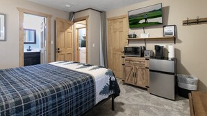 Ein Schlafzimmer mit einem Bett, einem Holzschrank, einer Mikrowelle, einem Kühlschrank und einer kleinen Küchenzeile.