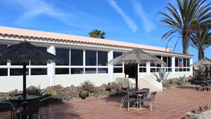 Un espace patio avec des sièges d’extérieur, une piscine et un bâtiment doté d’un toit et de fenêtres recouverts de tuiles.