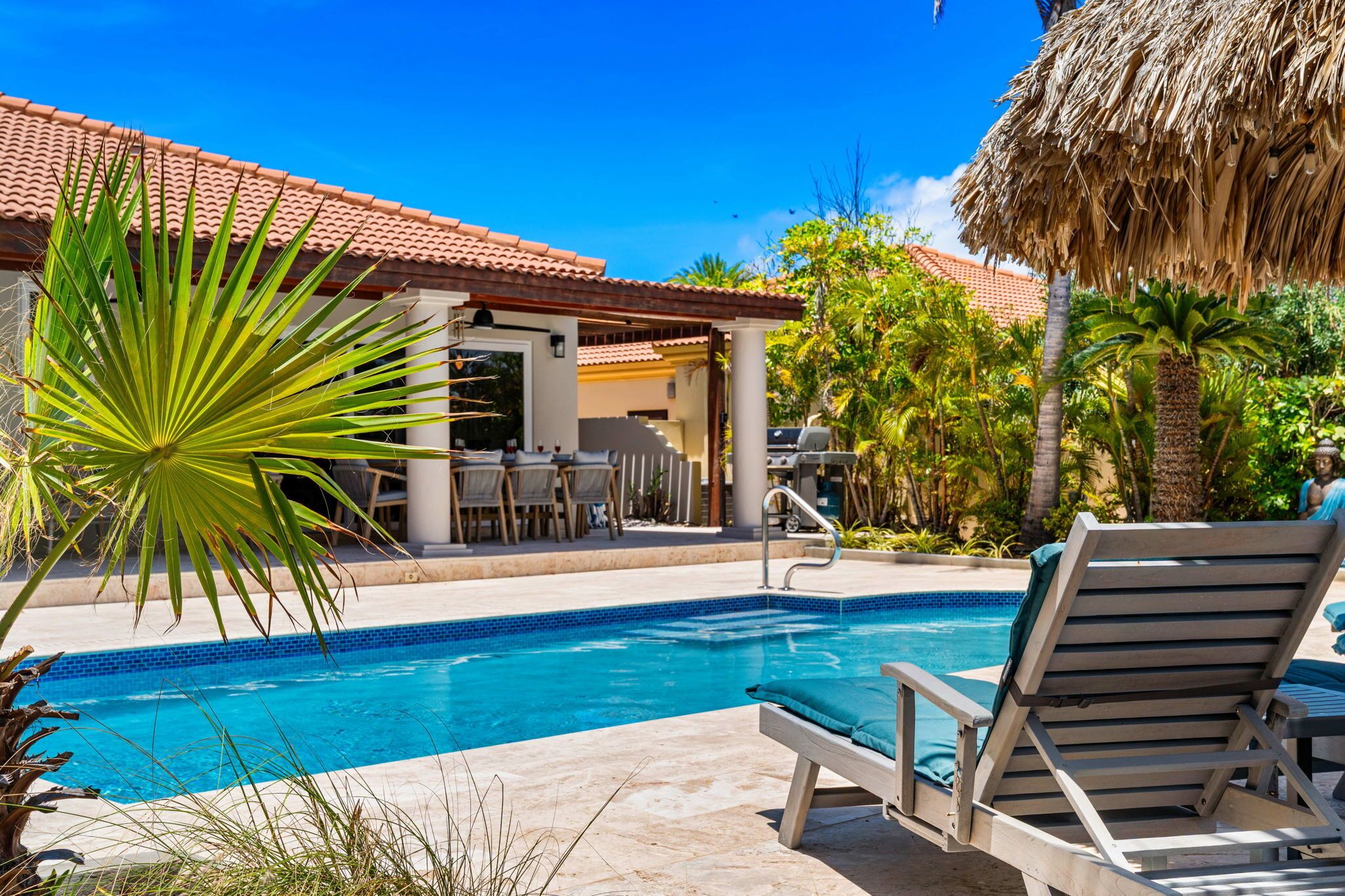 Una piscina con sillas de descanso, un porche cubierto y exuberante vegetación tropical.