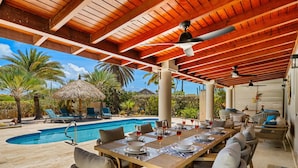 An outdoor pool area with a covered dining space, lounge chairs, and a thatched-roof structure. - Golfcourse Tropical Guest House Private Pool in Tierra del Sol! (Noord)