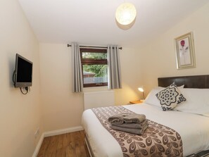 A bedroom with a bed, a television mounted on the wall, a window with curtains, a bedside lamp, and a framed picture on the wall.