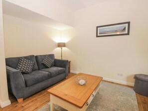 A living room with a grey sofa, two patterned cushions, a wooden coffee table, a floor lamp, and a framed picture on the wall.