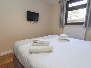 A hotel room with a bed, a TV mounted on the wall, and a window with curtains.