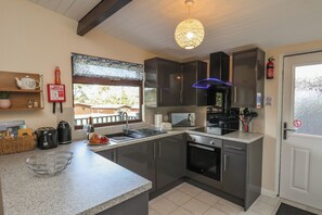 A modern kitchen with dark cabinets, a stainless steel range, and a large window. - Bugle (Saltburn-by-the-Sea)