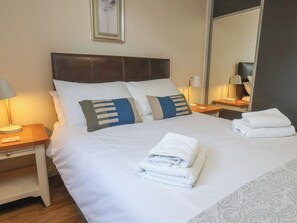 Habitación de hotel con cama, dos mesitas de noche, una lámpara, una toalla doblada y un espejo.