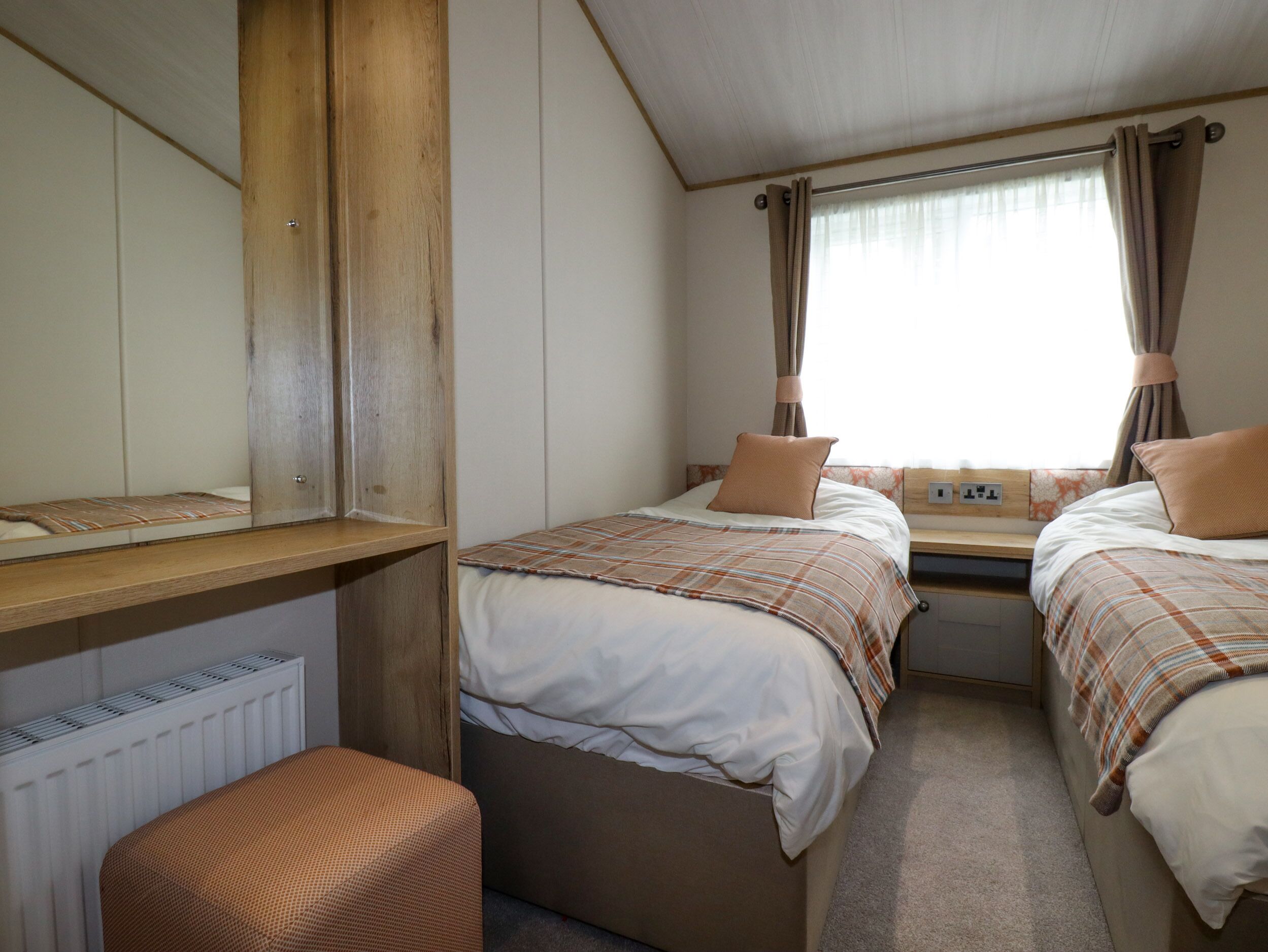 A compact room with two beds, a wooden bench, and a window with curtains.