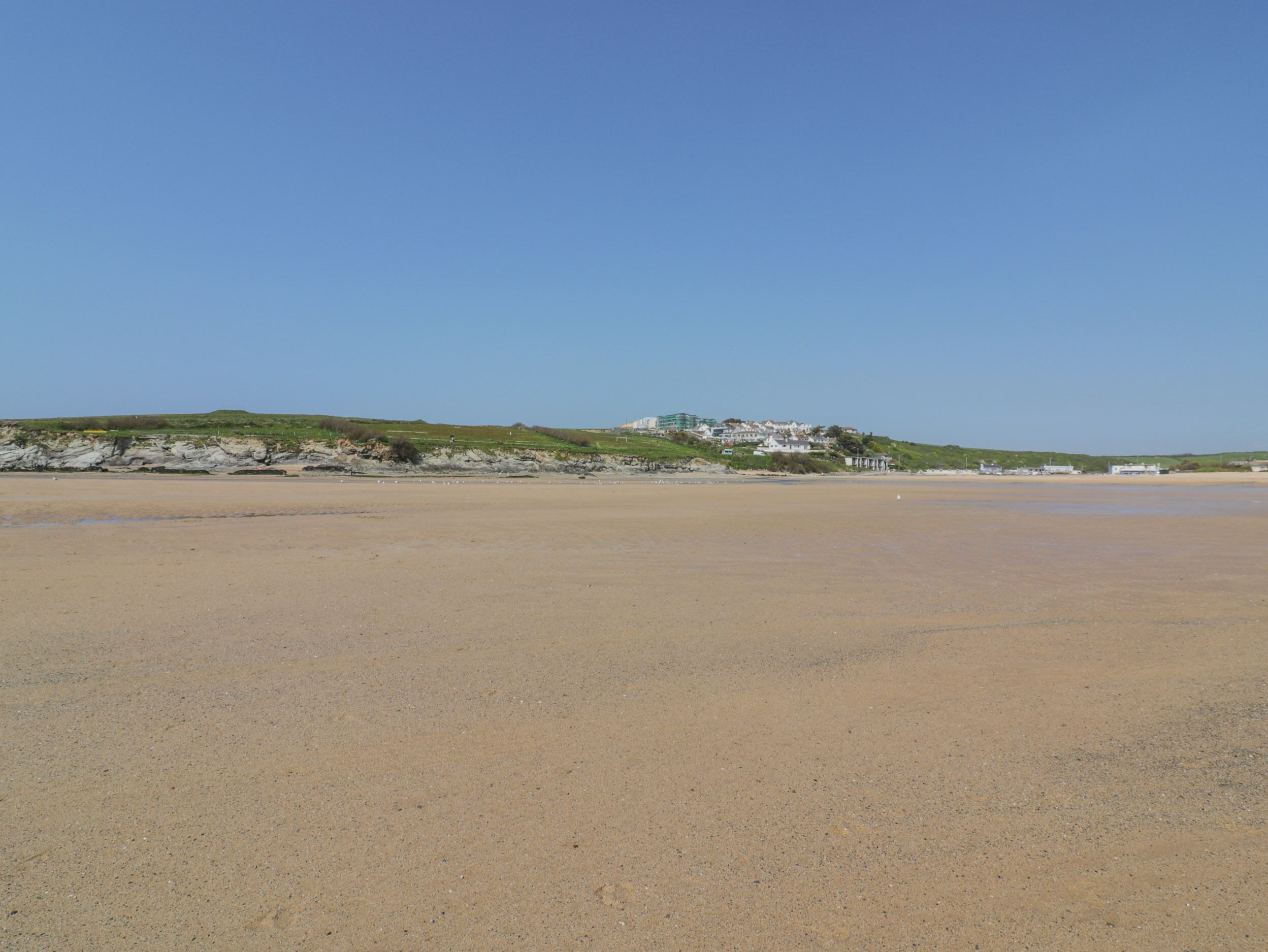 Een breed zandstrand met een rotsachtige uitstulping en gebouwen op de achtergrond.