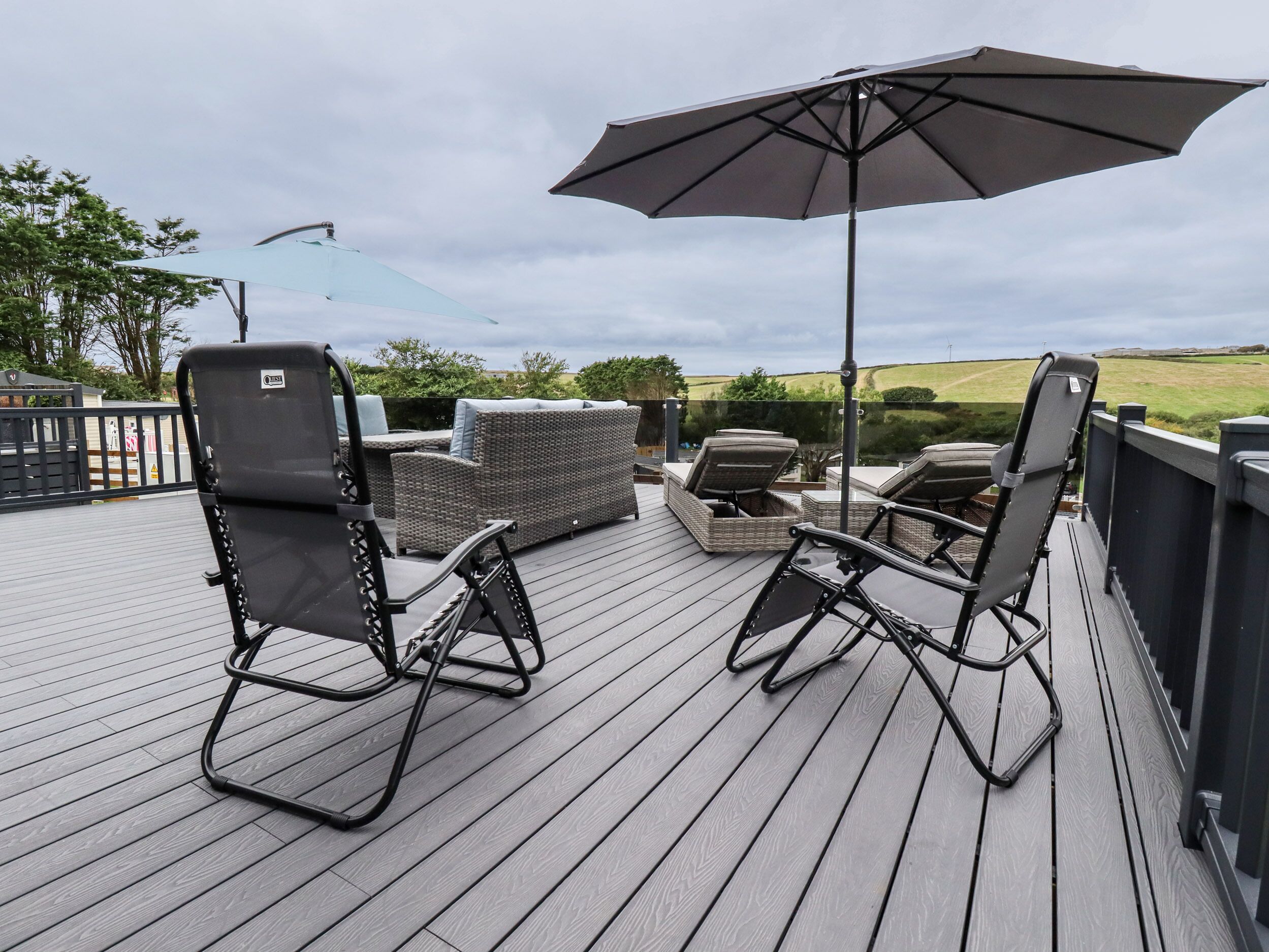 A deck with outdoor furniture including chairs and a sofa, a large umbrella, and a view of the countryside.