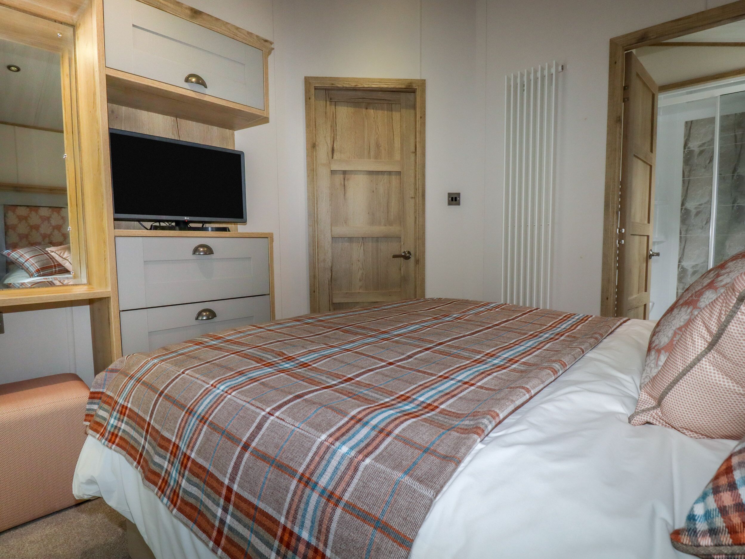 A bedroom with a bed, a television on a wooden cabinet, a wooden door, and a radiator.