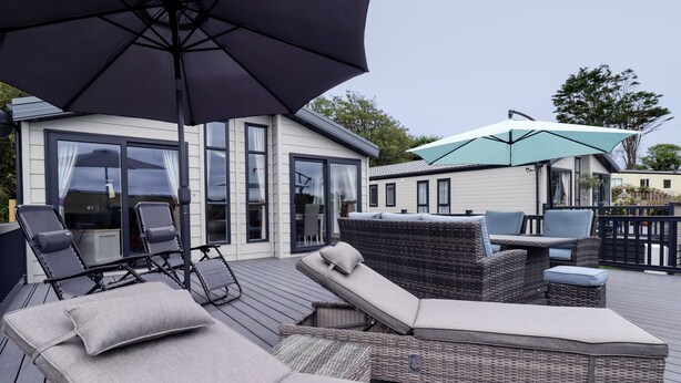 A covered outdoor seating area with lounge chairs and a table, surrounded by a deck and a building with large windows.