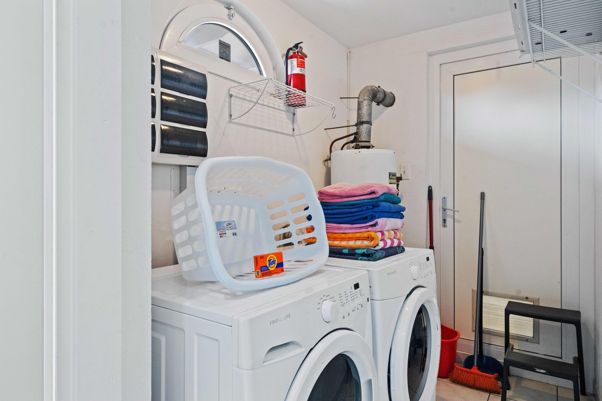 A laundry area with a washing machine, a dryer, a fire extinguisher, a mop, and a stack of folded towels.