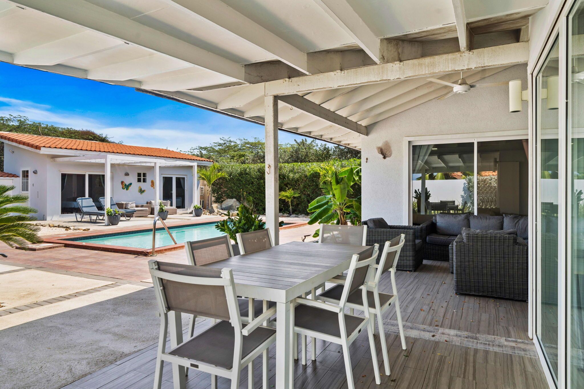 Un patio couvert avec une piscine, du mobilier d’extérieur et une vue sur une maison avec un toit rouge.