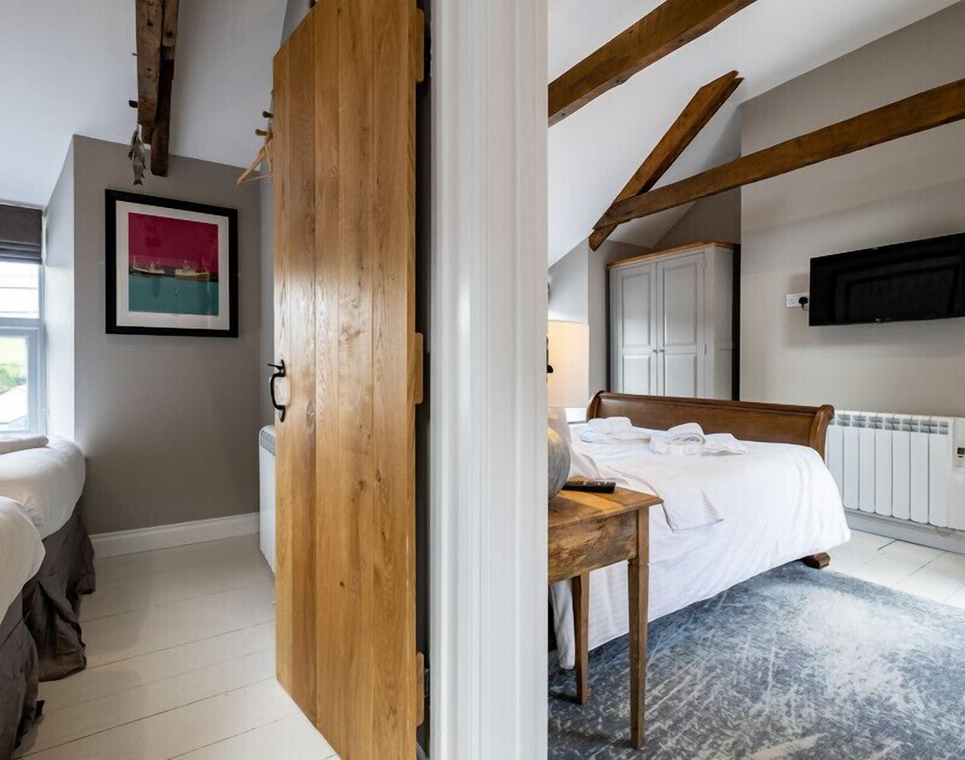 A bedroom with a bed, a wooden door, a desk, a chair, a radiator, and a framed picture on the wall.