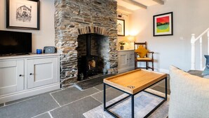 A living room with a stone fireplace, a television, and a wooden coffee table. - Mino Cottage (Port Isaac)