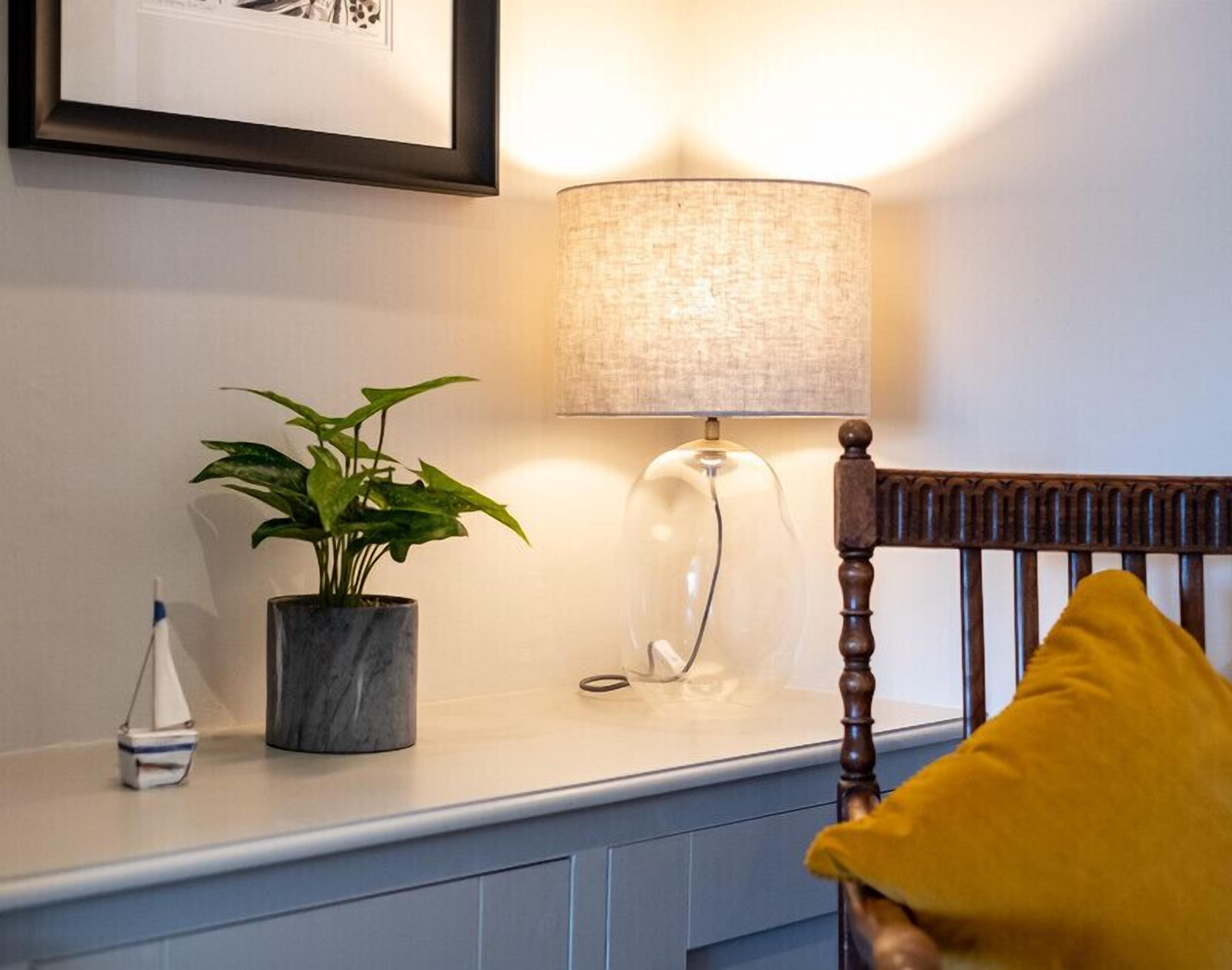 Une chambre avec une table de chevet, une lampe, une plante en pot et une chaise avec un coussin jaune.