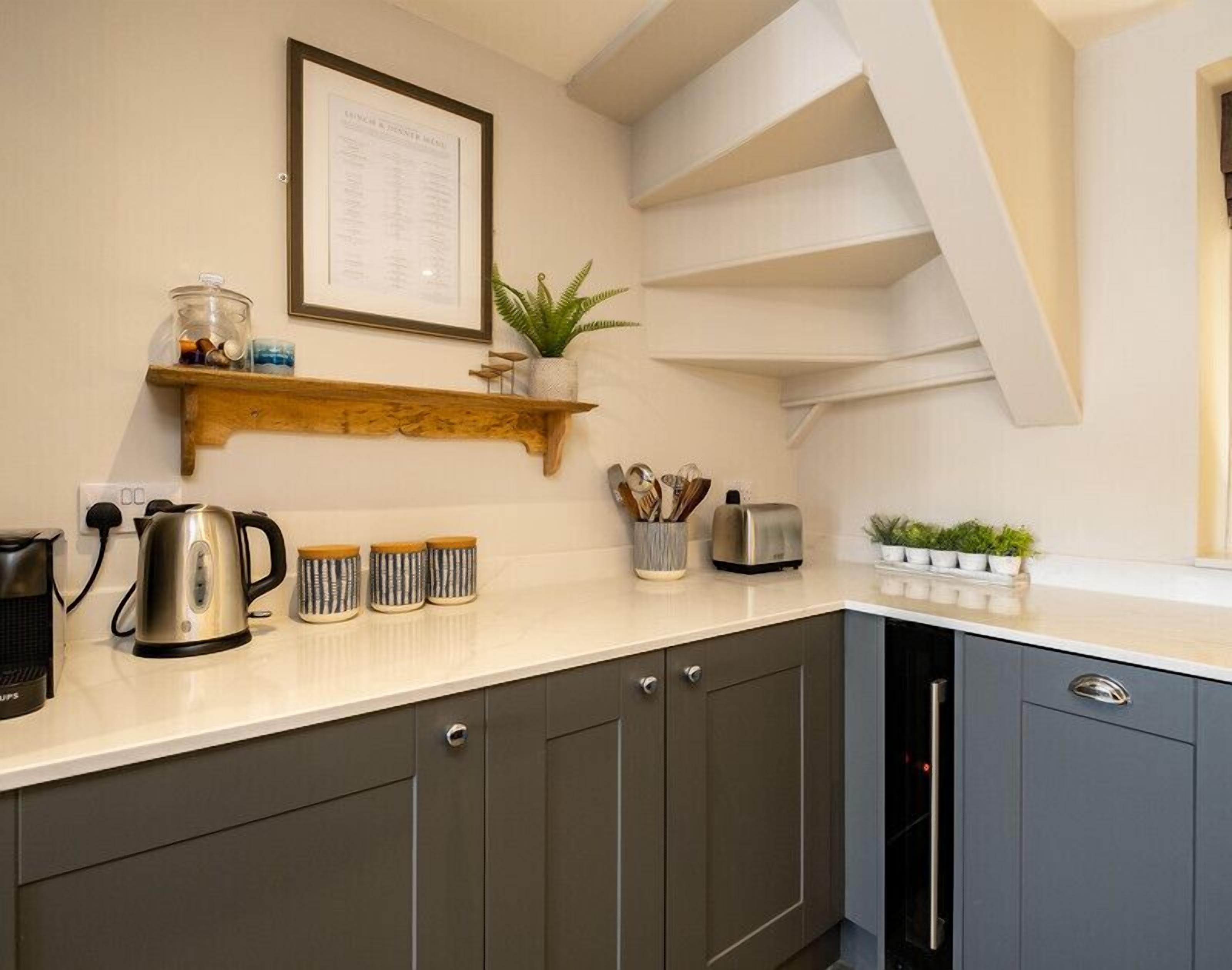 A modern kitchen with dark grey cabinets, a white countertop, a kettle, a toaster, and a plant on the shelf.
