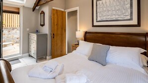 A bedroom with a large bed, a wooden headboard, a framed artwork on the wall, a dresser, and a door leading to an outdoor area. - Mino Cottage (Port Isaac)