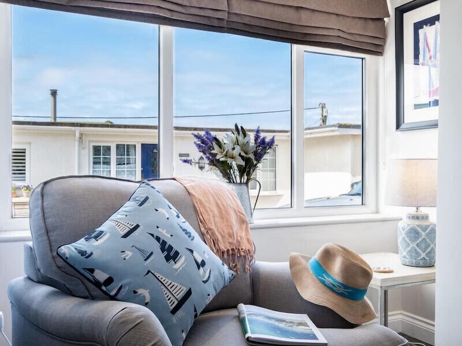 Een gezellige kamer met een grijze fauteuil, een blauw kussen met patroon, een hoed en een vaas met bloemen.