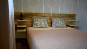 Une chambre à coucher avec un lit, deux coussins à motifs, une table de chevet et une lampe fixée au mur.