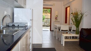 Une cuisine moderne équipée d’une cuisinière intégrée, d’un évier et de placards. On y trouve également un coin repas avec une table et des chaises, ainsi qu’un salon avec un canapé et un vase rempli de plantes.