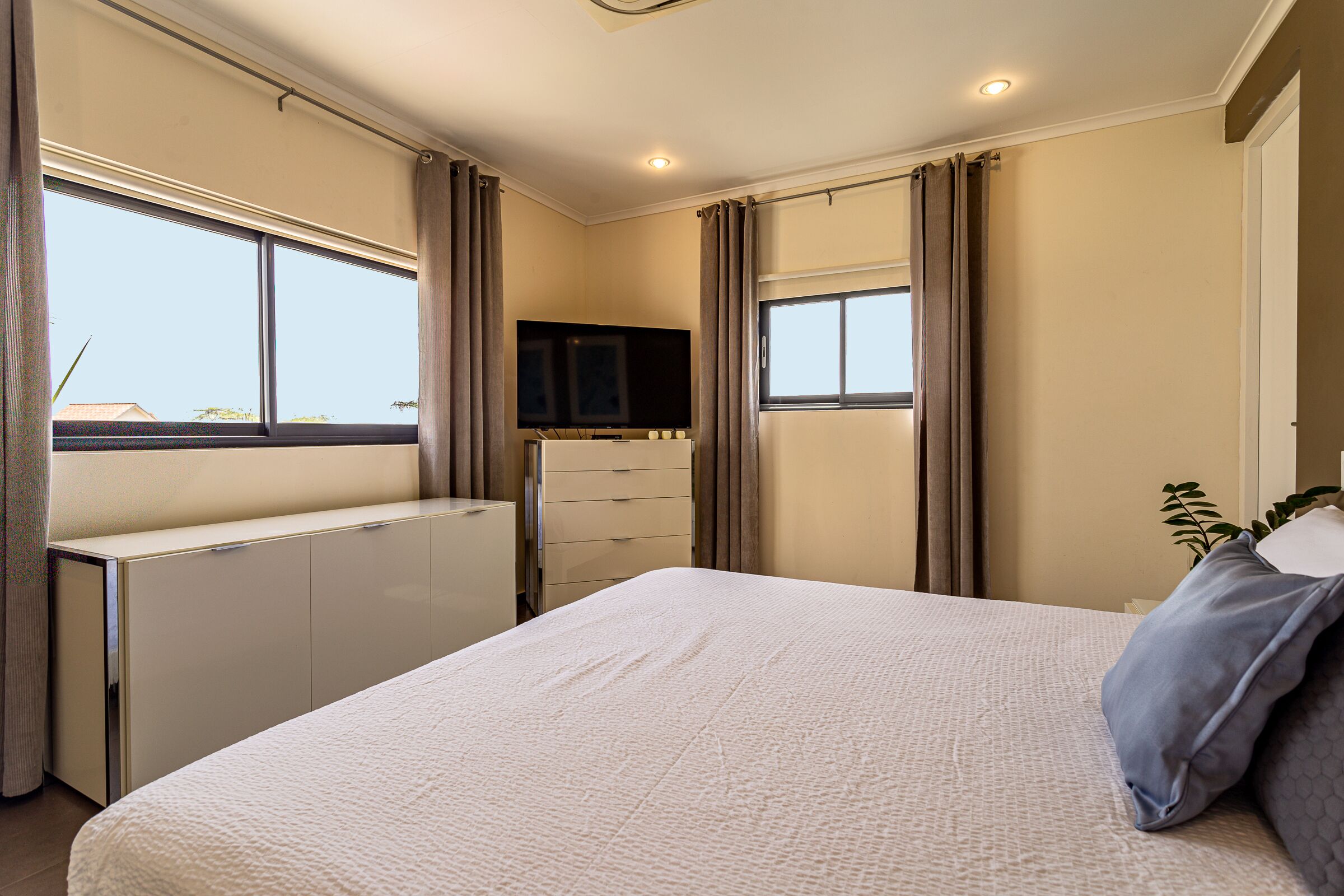 Una camera da letto con un letto, una cassettiera, una televisione e finestre con tende.