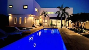 Ett modernt hus med en swimmingpool i skymningen.