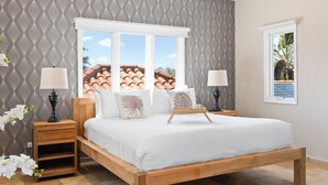 Un dormitorio con cama, dos mesitas de noche, una ventana con vistas a un tejado de tejas y papel tapiz estampado.