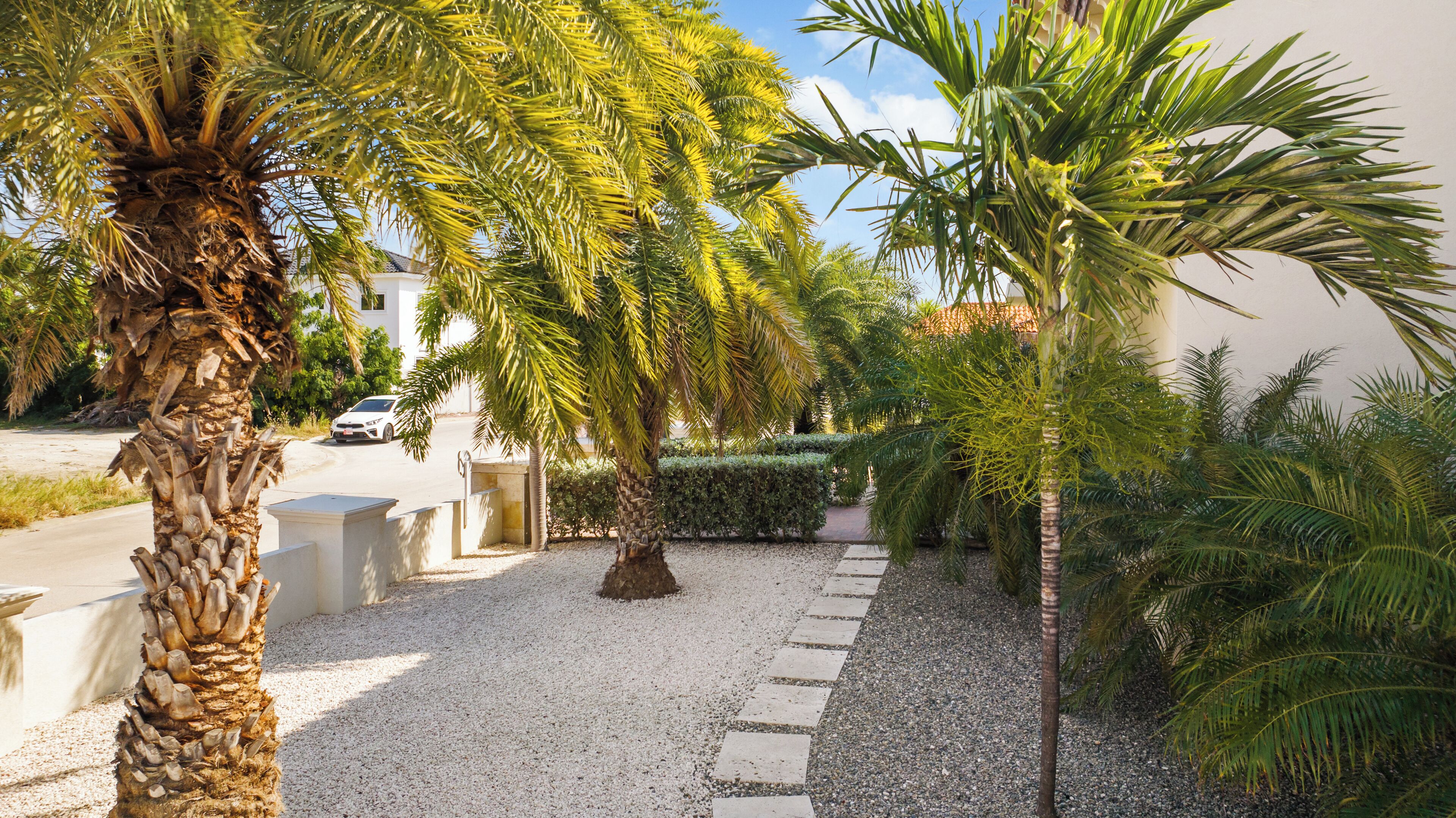 A gravel pathway leading to a white building with a car parked in the background.