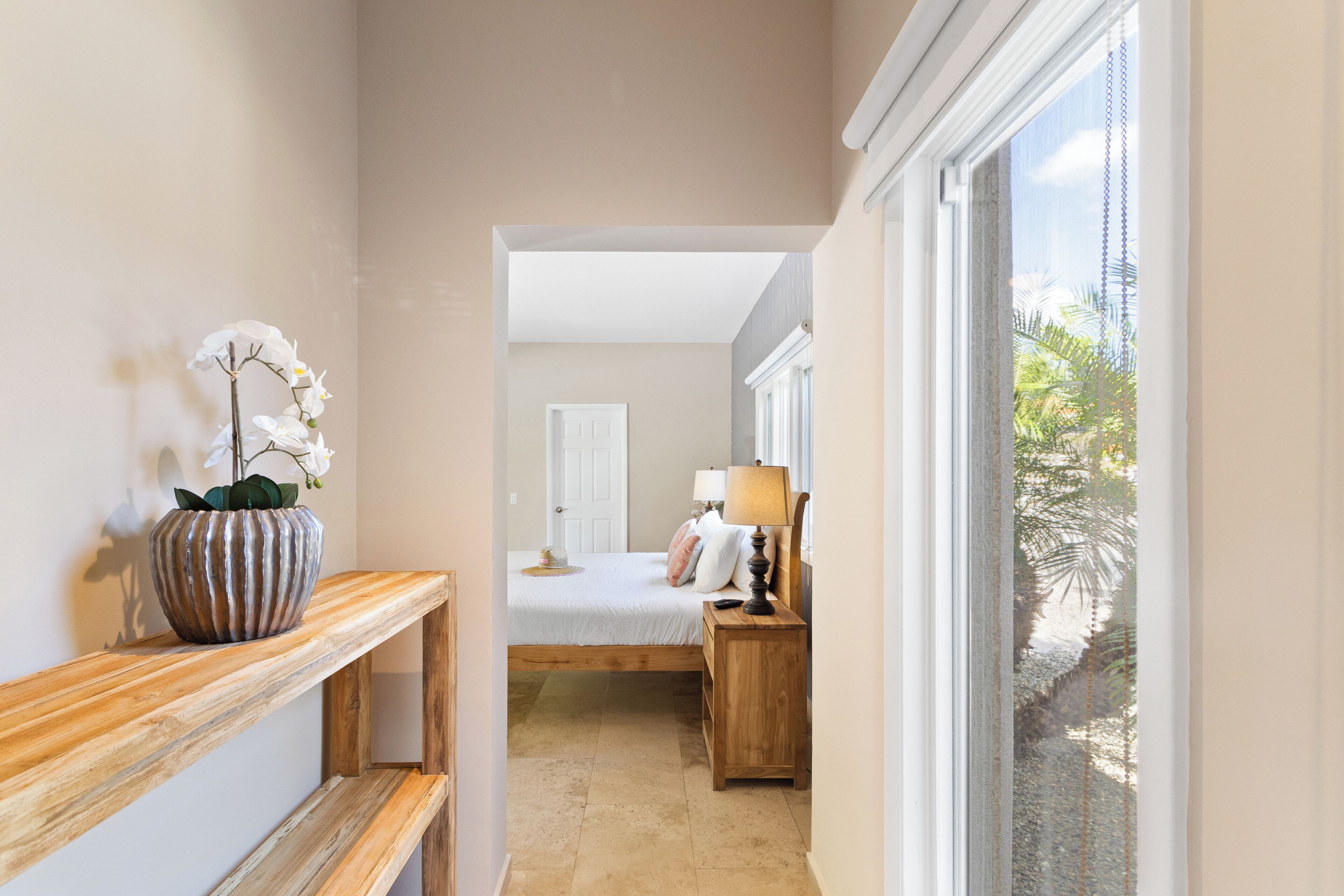 Een gang die leidt naar een slaapkamer met een bed, nachtkastje, lamp en een potorkidee.