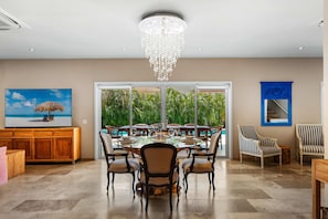 Uma sala de jantar com uma mesa grande, cadeiras, um lustre e vista através de portas de vidro.