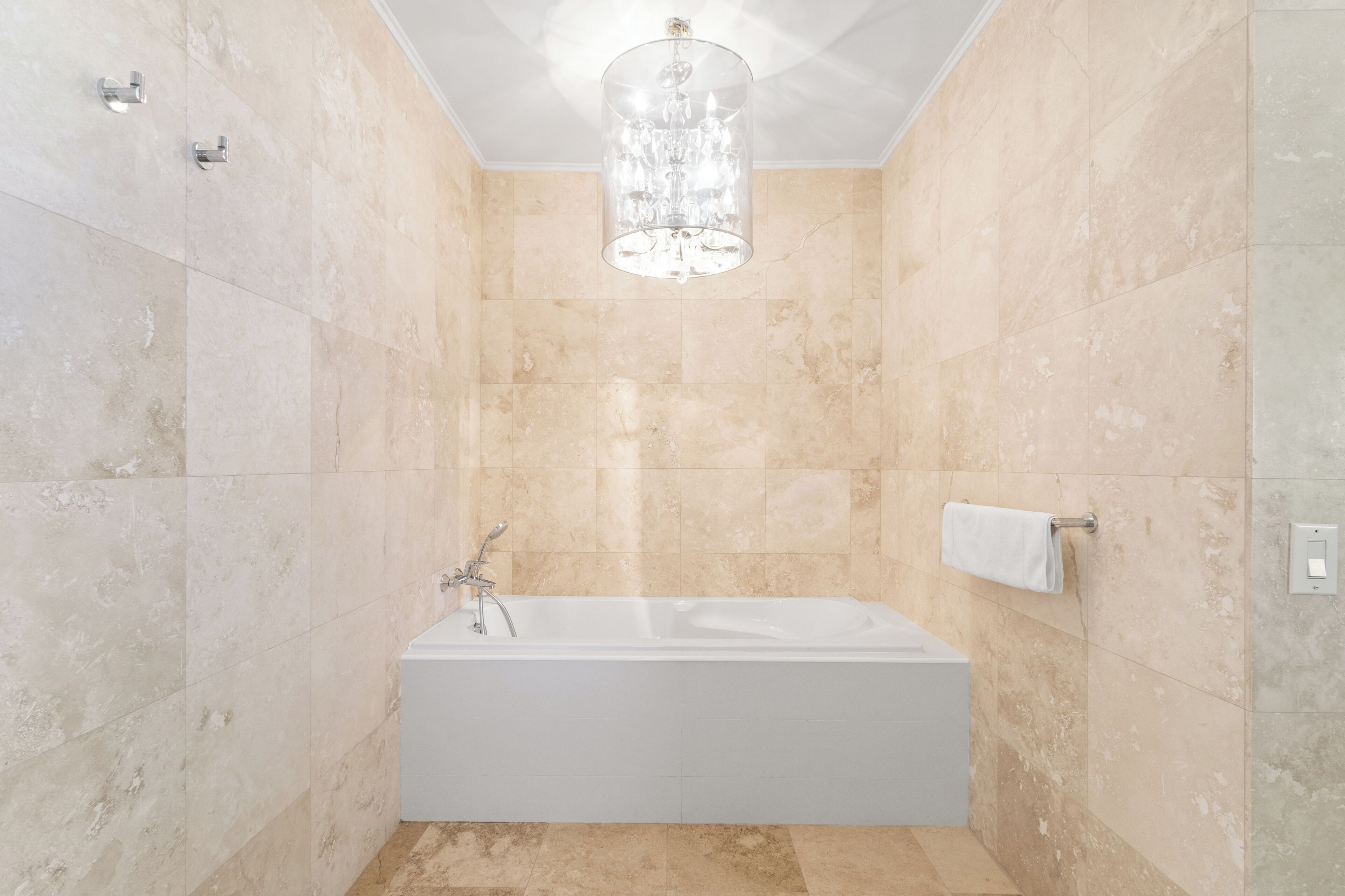 A modern bathroom with a freestanding bathtub, a chandelier, and a towel rack.