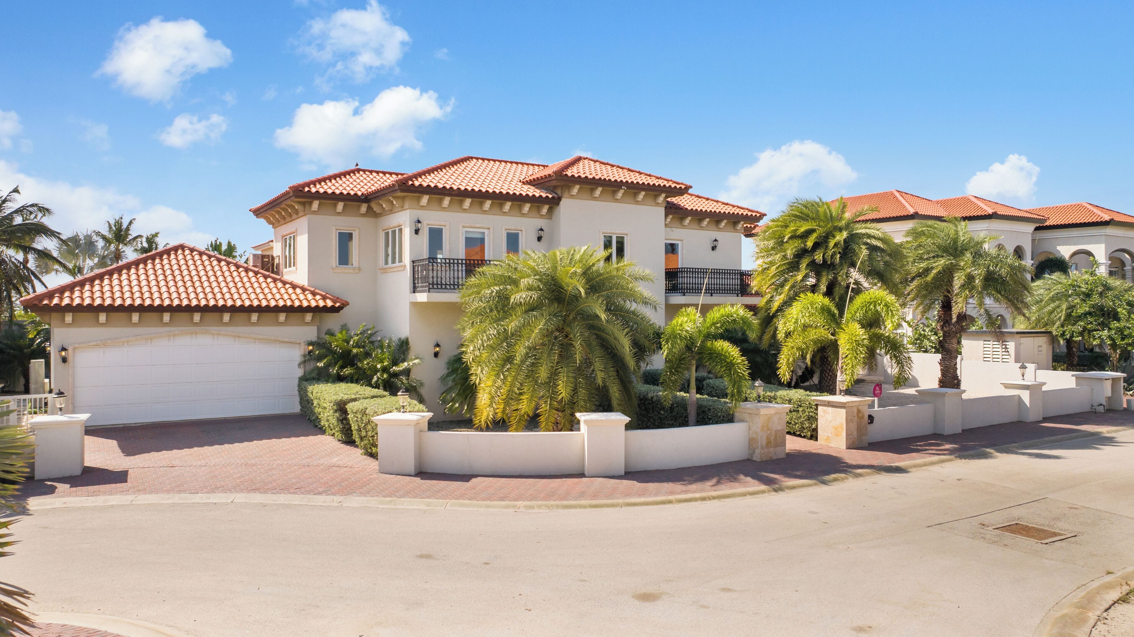 A multi-story residential building with a red-tiled roof, a white garage, and a landscaped front yard with palm trees.