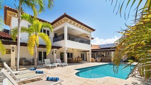 Una casa de dos pisos con piscina, mobiliario exterior y palmeras.