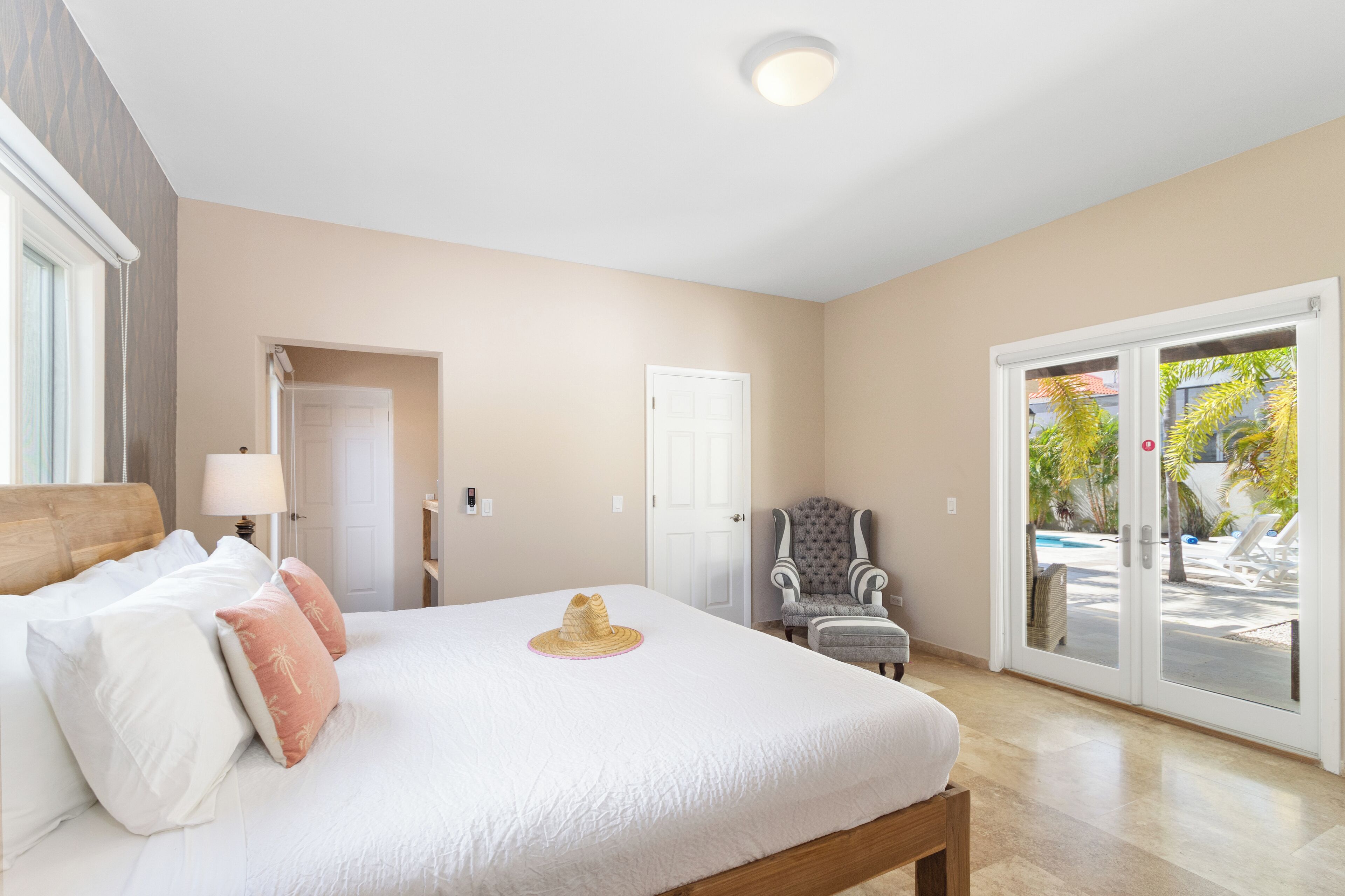 Une chambre spacieuse avec un grand lit, un fauteuil et une vue sur la piscine, accessible par une porte-fenêtre coulissante.