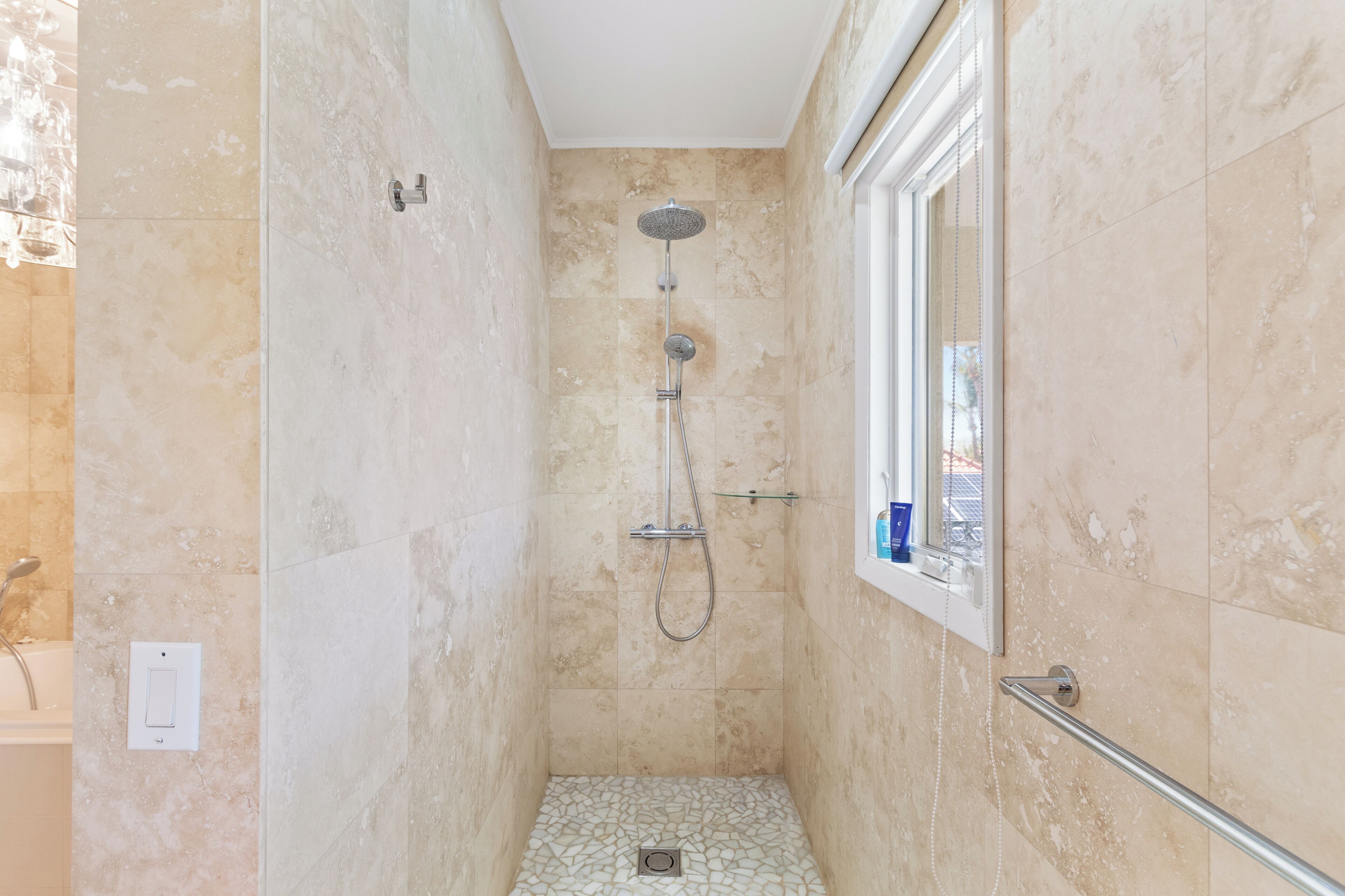 Une douche à l’italienne avec une porte en verre, un pommeau de douche et un flexible de douche.