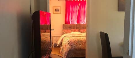 A bedroom with a bed, a bedside table with a lamp, a chair, and a television.