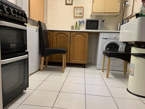 Une cuisine équipée d’une cuisinière, d’un four à micro-ondes, d’un lave-linge et d’une chaise.