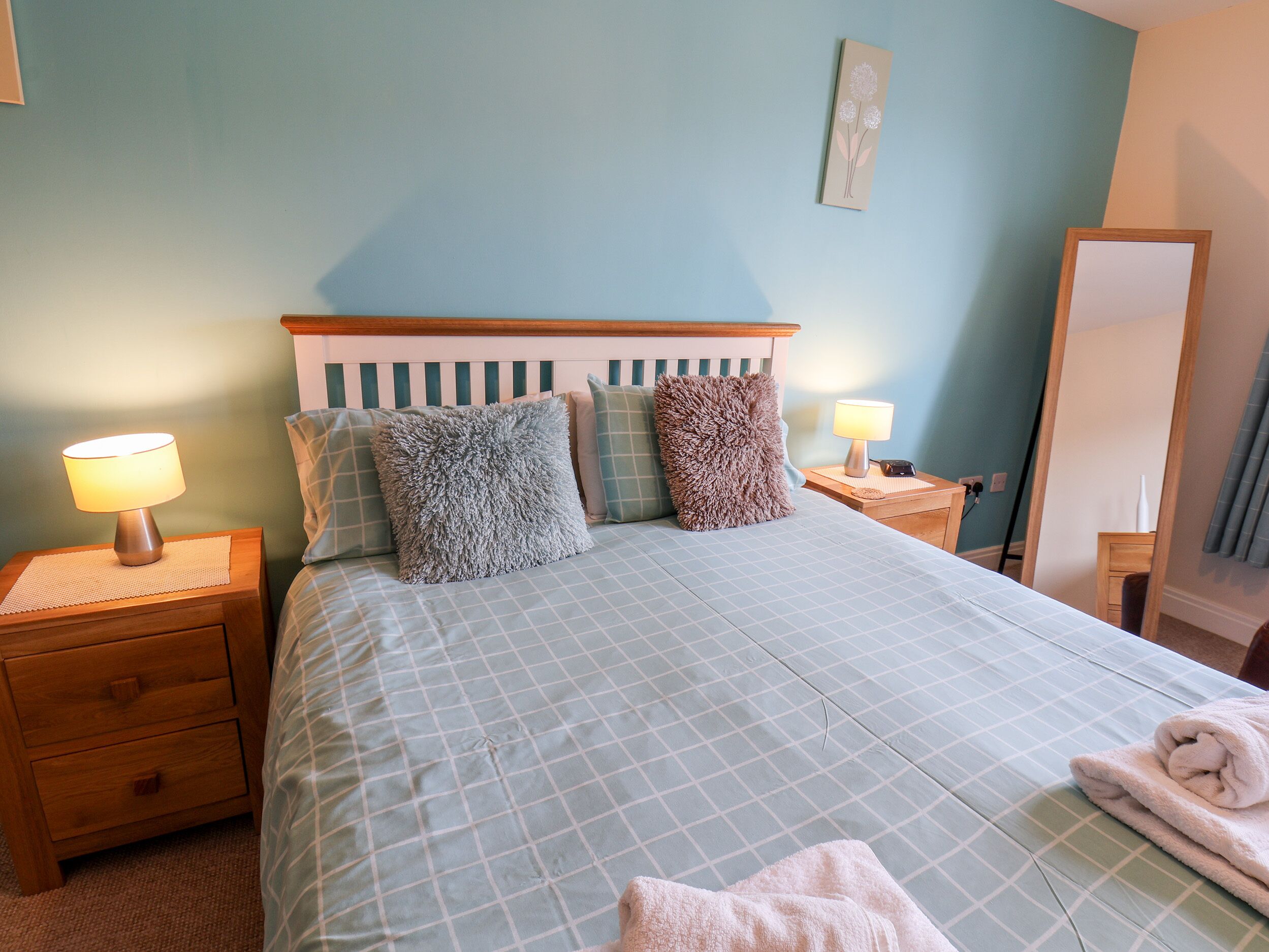 Une chambre à coucher comprenant un lit, deux tables de chevet, une commode, un miroir et un tableau accroché au mur.