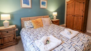 Een slaapkamer met een bed, twee nachtkastjes met lampen, een houten garderobe en twee ingelijste foto's aan de muur.