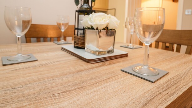 Een eettafel met vier wijnglazen, een wijnfles en een vaas met witte bloemen.
