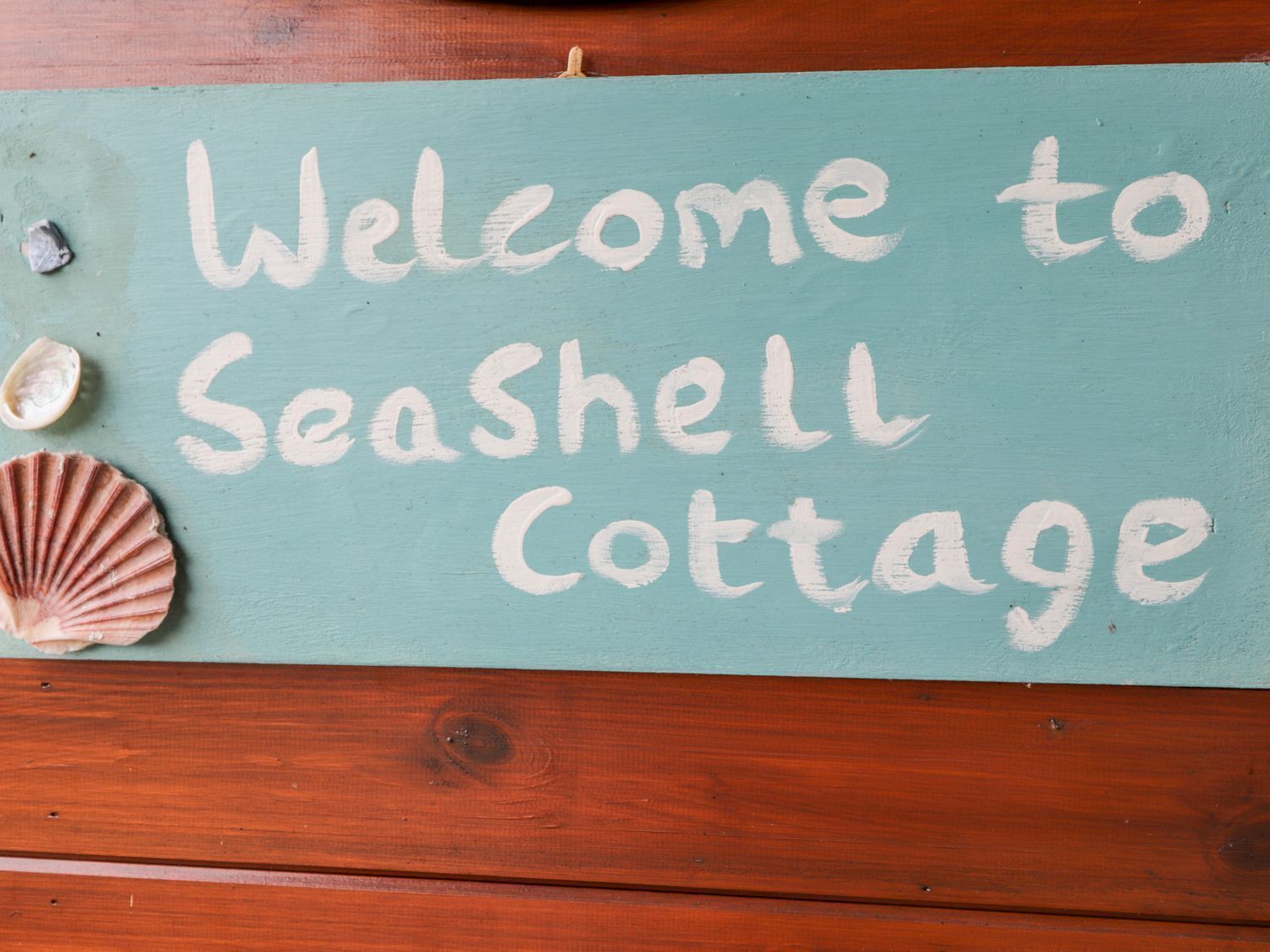 A sign with the text "Welcome to Seashell Cottage" and a seashell.