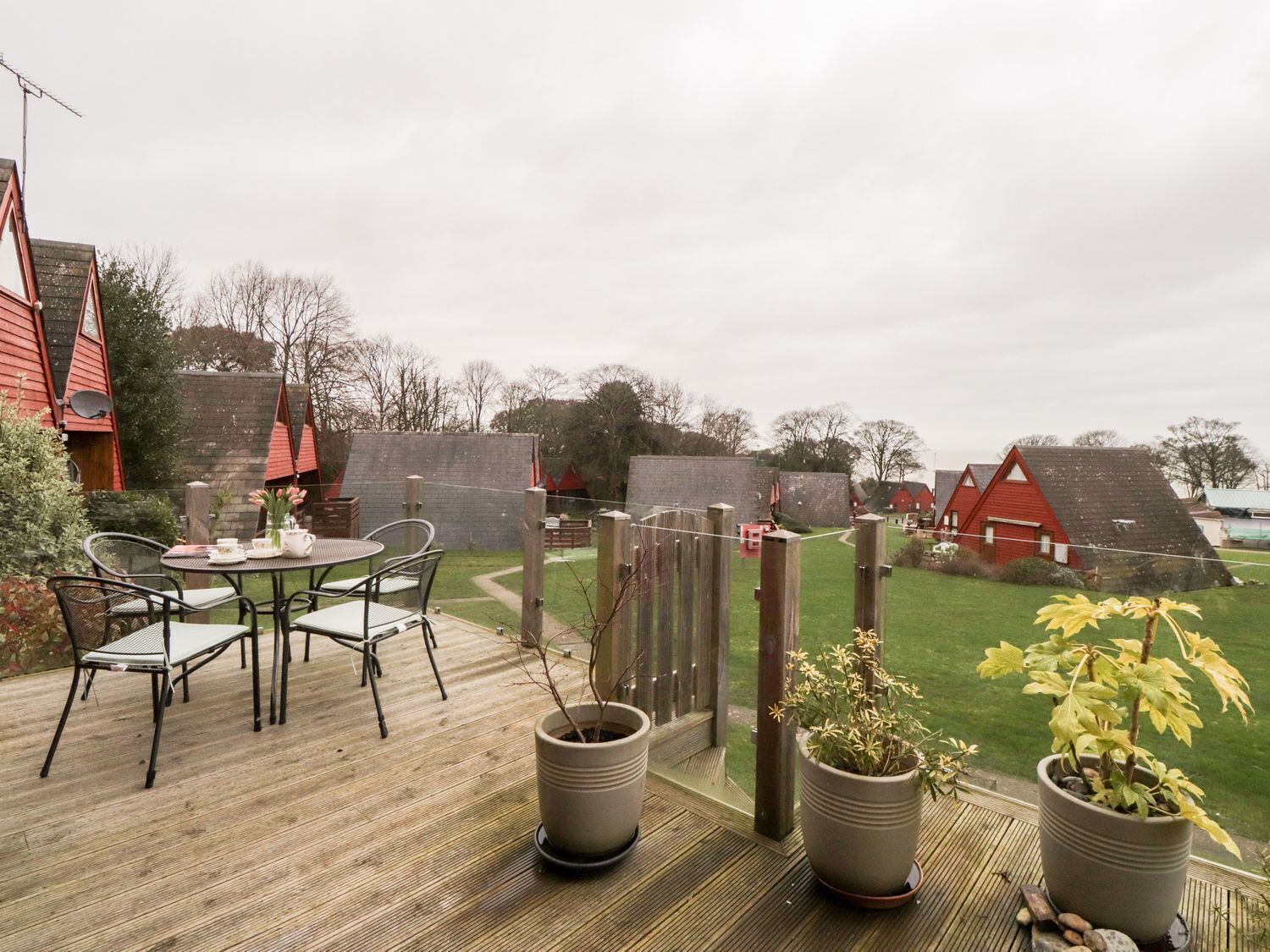 Una terraza de madera con una mesa y sillas, rodeada de plantas en macetas.