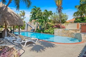 A swimming pool with lounge chairs, a palm tree, and a stone wall.