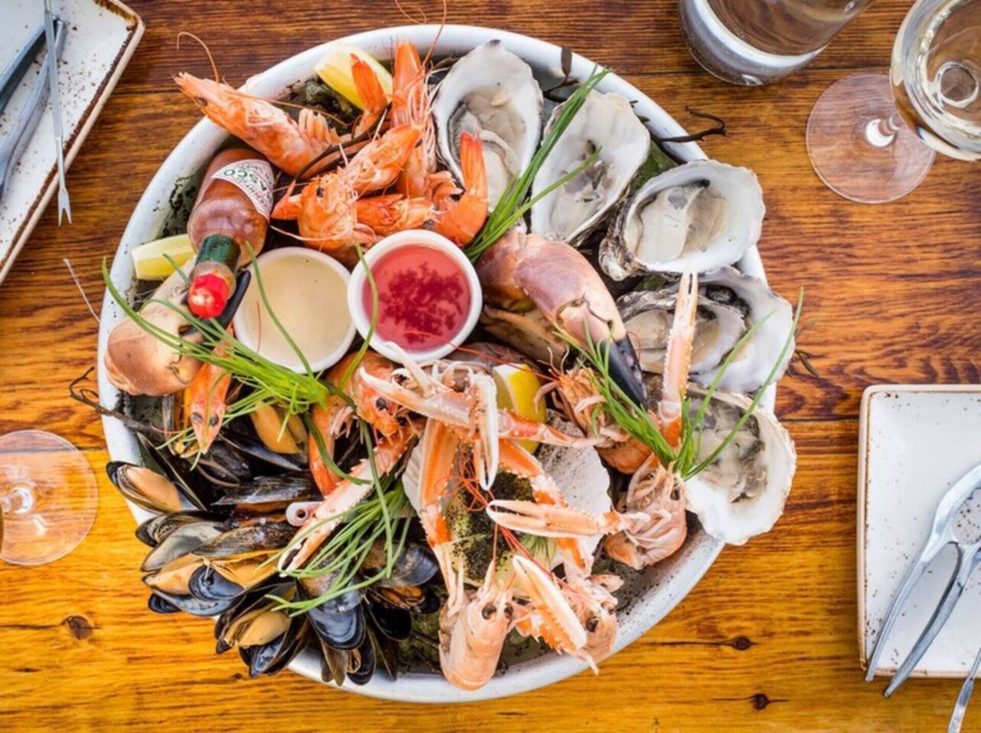 Un plateau de fruits de mer comprenant divers crustacés et crevettes, accompagné de quartiers de citron et de deux sauces pour tremper.