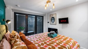 A bedroom with a bed, a TV, a window with blinds, and a ceiling light fixture. - Tiny House, Brighton With Parking (Brighton)