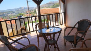 Un balcón con sillas de mimbre y una mesa de vidrio, con vistas a un paisaje montañoso.