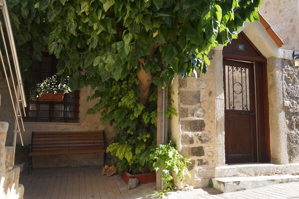 Un bâtiment en pierre avec un banc en bois, une plante en pot et une porte portant un numéro.