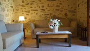Una sala de estar acogedora con una pared de piedra, un sofá color beige, una mesa de centro de madera con un cesto de flores y una lámpara.