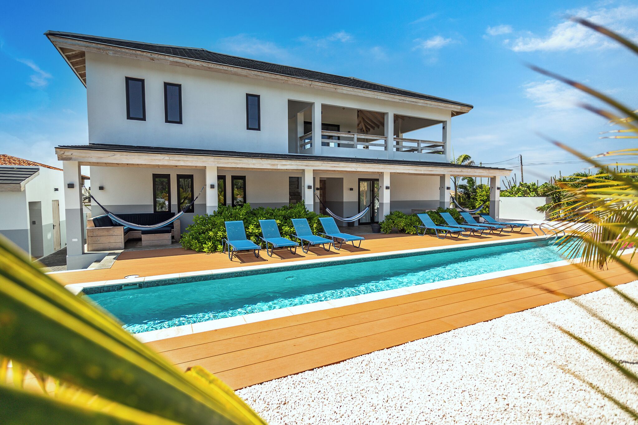 Ein zweistöckiges Haus mit Swimmingpool, Liegestühlen und einer Hängematte.