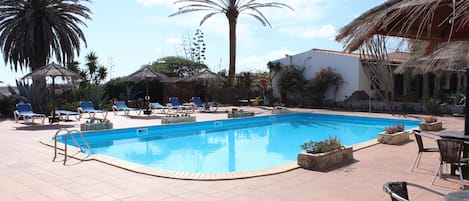 Una piscina con lettini e una struttura con tetto di paglia.